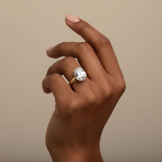 Model wearing an oversized oval cushion-cut crystal solitaire ring in a gold-tone four-prong setting